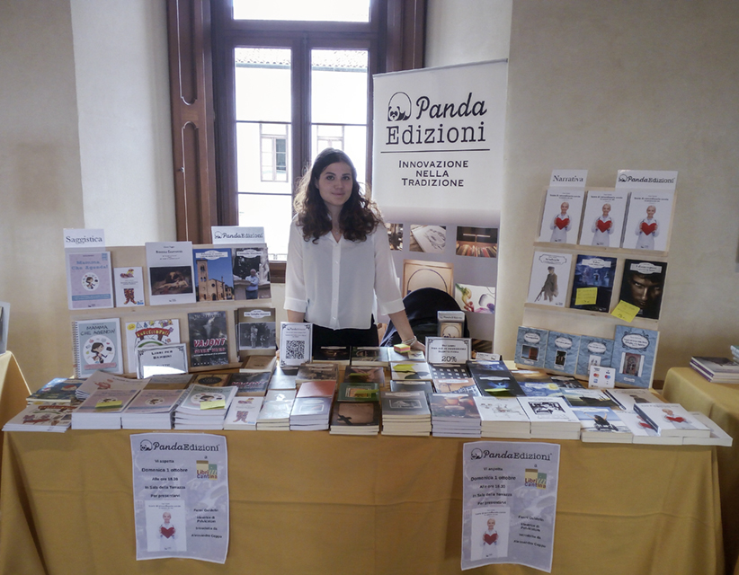 Editor Volpato (English-Italian-translator) standing behind a stand full of books during a bookfair.